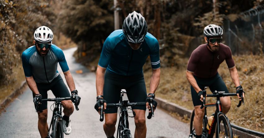 Exercise Bike Workouts - Group of bicyclists in sportswear and helmets riding on bicycles on asphalt road near forest and grass in daytime in countryside