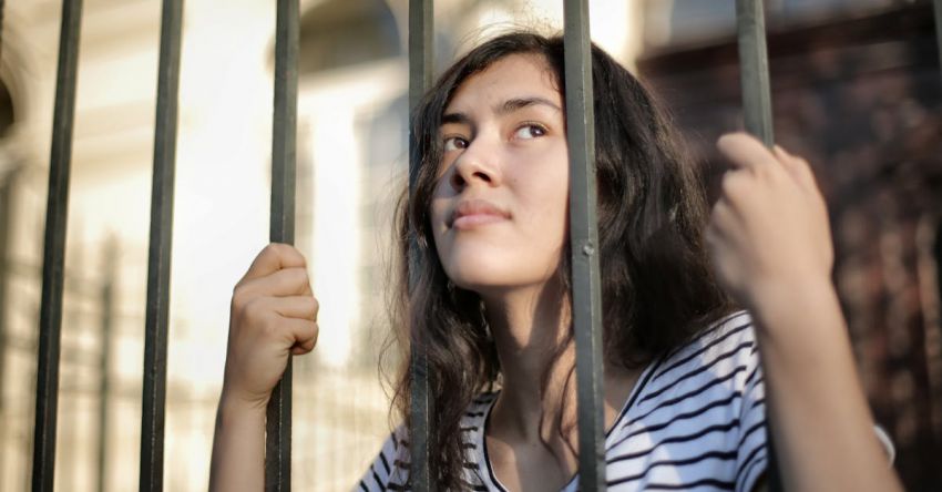 Pull-up Bars - Sad isolated young woman looking away through fence with hope