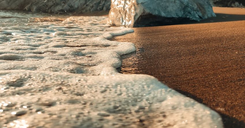 Foam Rollers - A rock on the beach with waves coming in